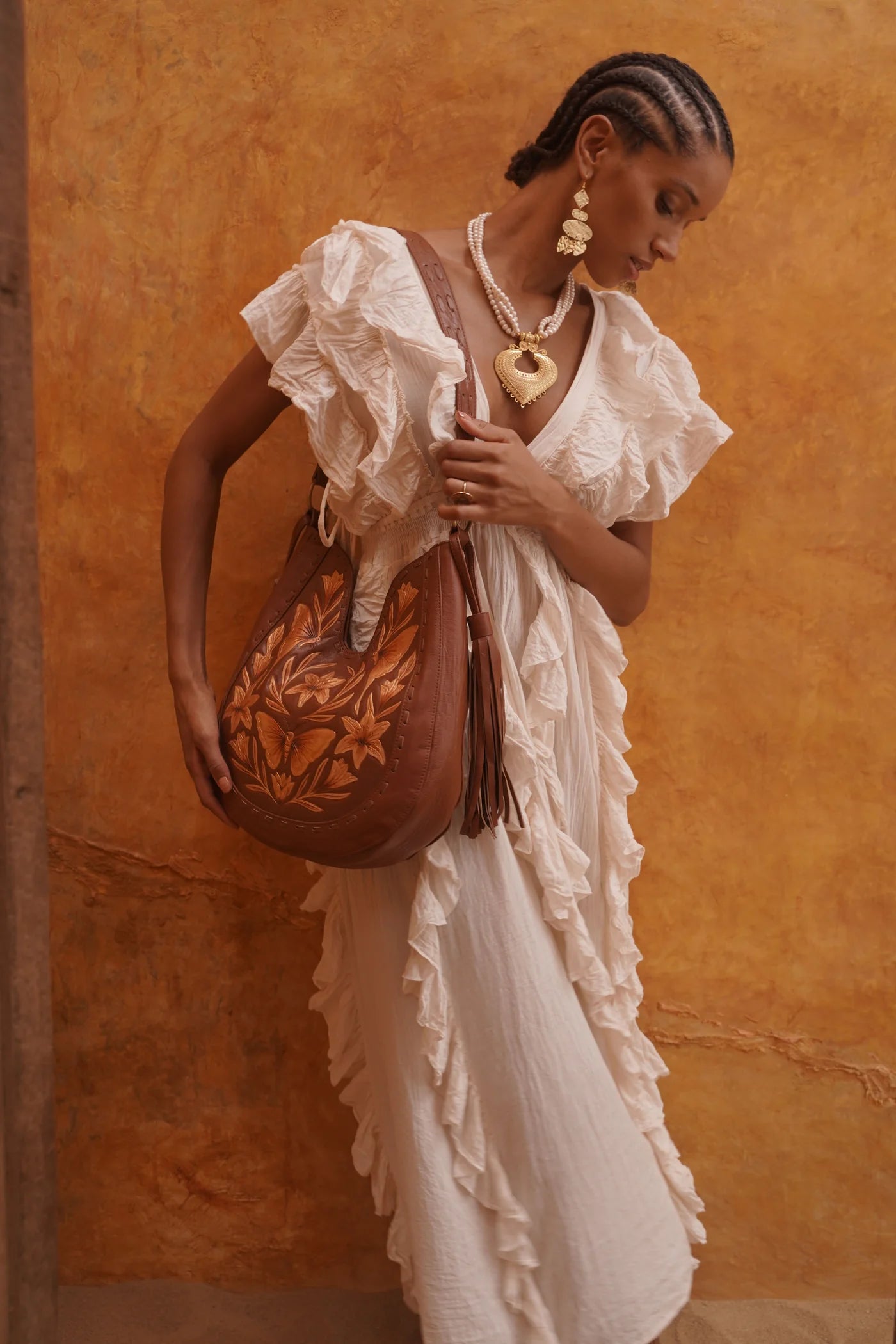 Woman in a white dress holding a brown leather bag against an orange wall