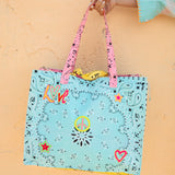 A light blue bandana-patterned tote bag with pink handles. The bag features colorful embroidered details including hearts, stars, a peace sign, and the word 'LOVE'.