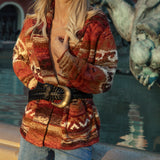 A woman wearing a rust-red and beige patterned knit cardigan with a black braided belt and gold buckle, paired with Paris Denim Jean